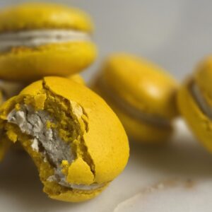 Close-up of yellow macarons with white filling; a bite reveals the crumbly interior. (informative dessert image)