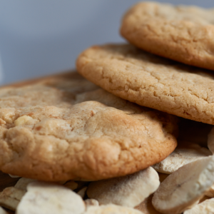 Stack of golden cookies resting on a wooden surface with cookie crumbs scattered nearby, close-up view.